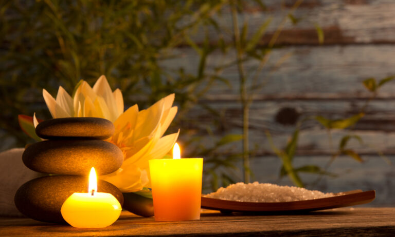 A table with a candle light a plate of salt , herbal flower, stone and a towel