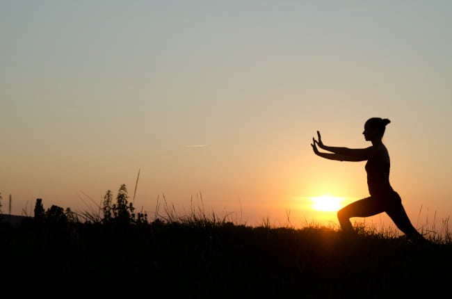 A lady doing a tai chi in front of a sunset