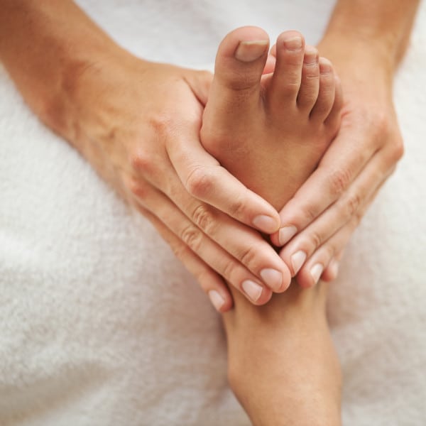 A hand of a massage therapist doing a reflexology massage to the right foot