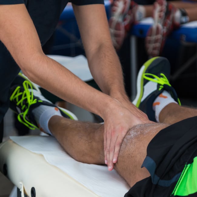 A masseur doing a massage on the left upper knee of an athlete