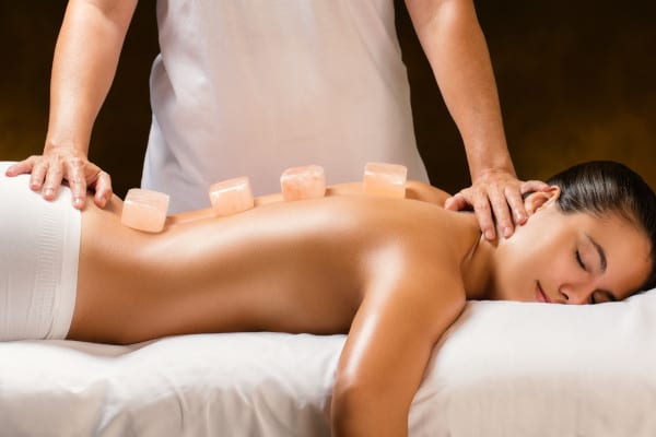 A woman laying on a bed and having a Himalayan hot stone massage