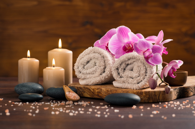 A massage wood tray with a massage towels, candles a massage stones a cup and an orchid