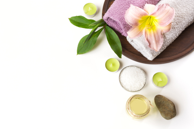 A massage wood tray with towels a candles a herbal flower a massage stone and massage oil