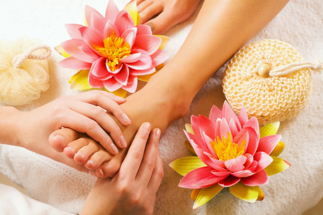A left foot of a lady placed on a white towel with a herbal flower and a sponge